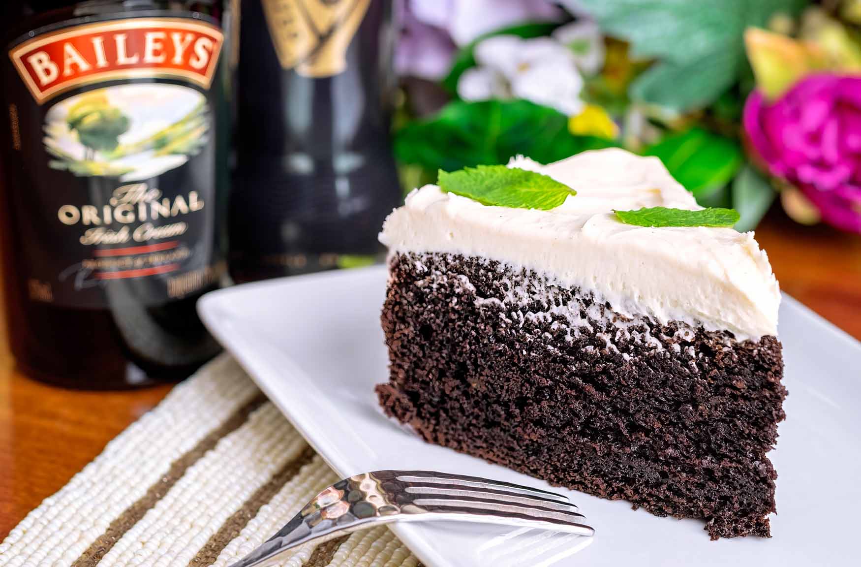A slice of Guinness Chocolate Cake on a plate near a bottle of Baileys Irish Cream.